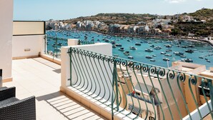 A balcony with a view of a marina filled with boats, overlooking a coastal town with buildings and hills. - Xemxija Bay Hotel (St. Paul's Bay)