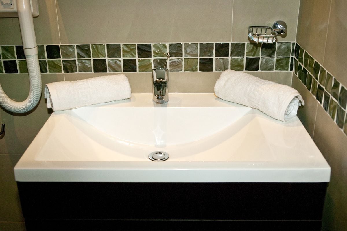 Un baño con un lavamanos blanco, dos toallas y un salpicadero de azulejos.