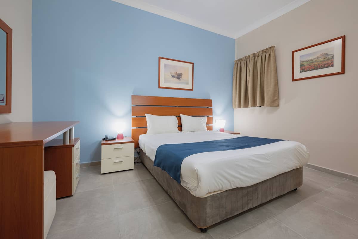 Een slaapkamer met een houten bed, een nachtkastje, een bureau en twee ingelijste foto's aan de muur.