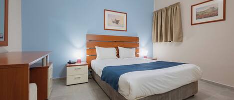 A bedroom with a wooden bed, a nightstand, a desk, and two framed pictures on the walls.