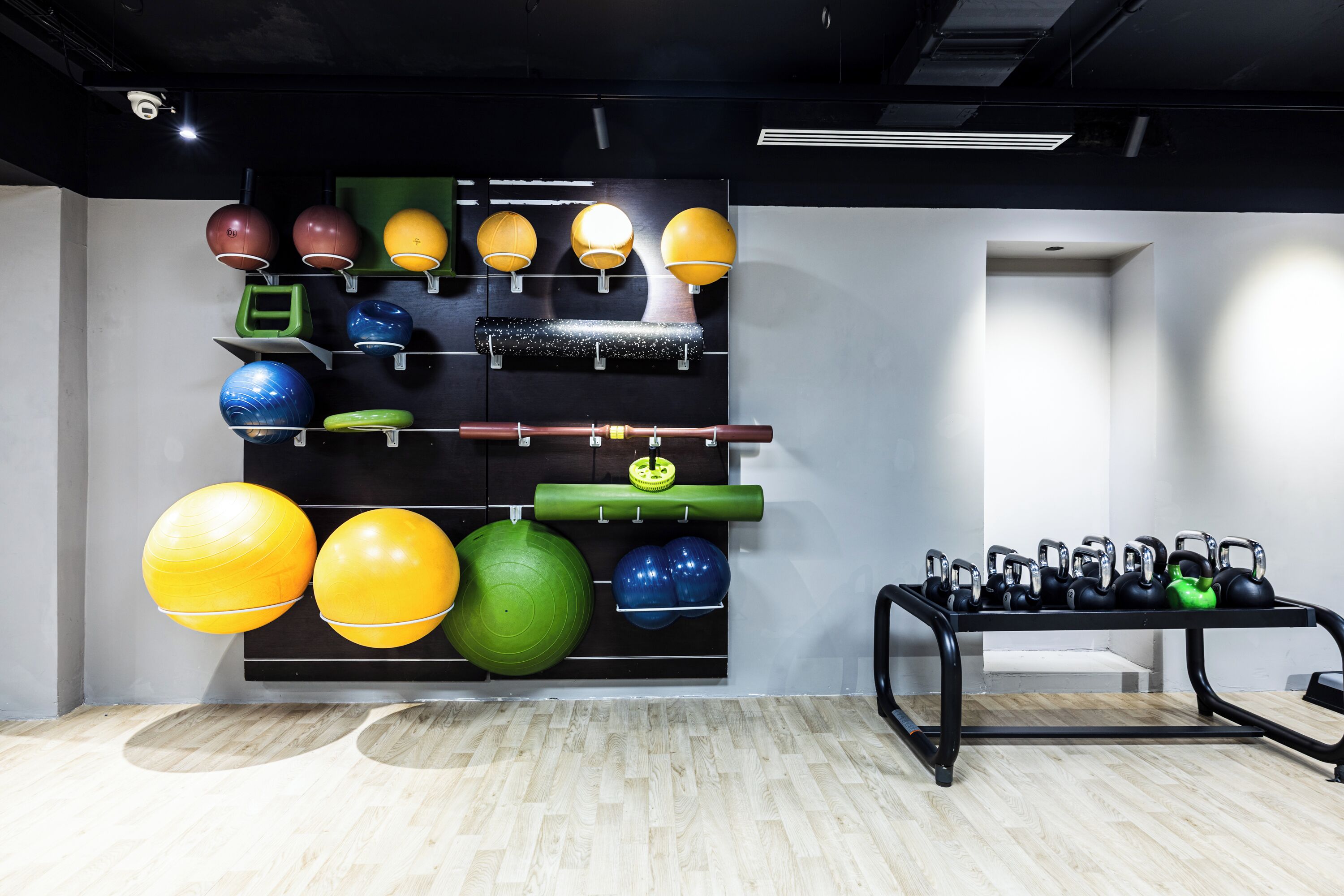 Un gimnasio con equipo de ejercicio, un estante en la pared con pelotas de fitness y pesas de kettlebell sobre una mesa.