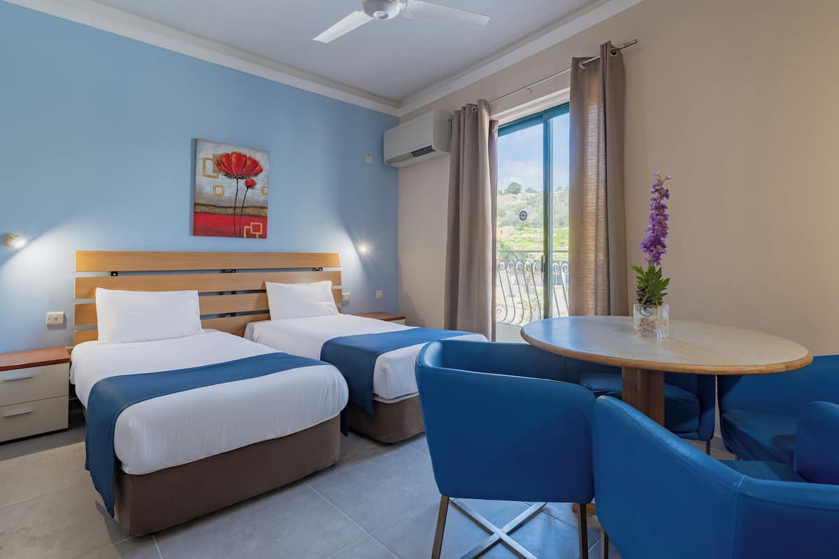 Een hotelkamer met twee bedden, een eettafel met blauwe stoelen, een plafondventilator en een raam met gordijnen.