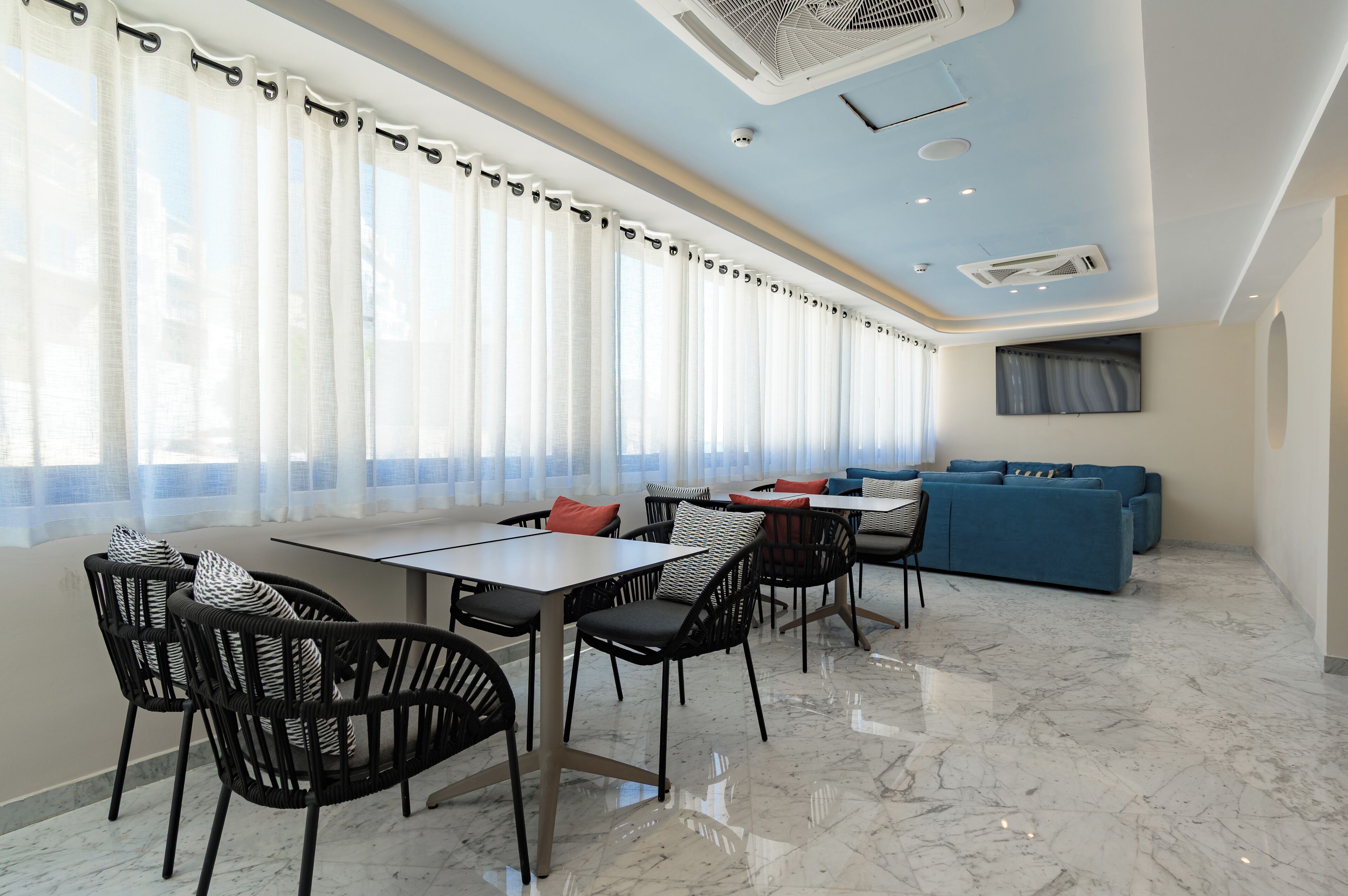 A modern dining area with a long table and chairs, a blue sofa, and a large window with sheer curtains.
