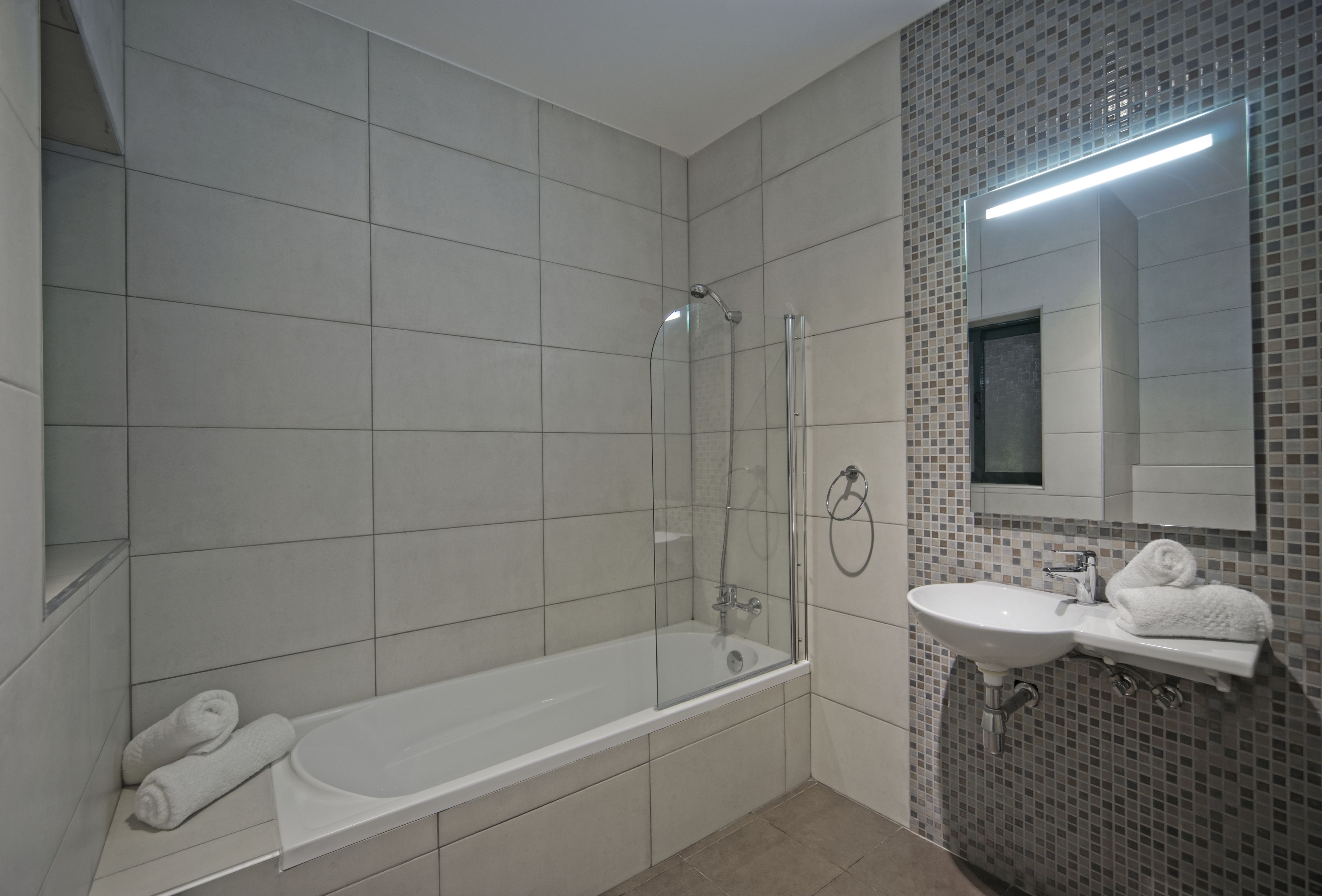 A bathroom with a bathtub, a glass-enclosed shower, a sink, and a mirror.