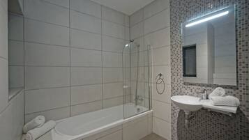 A bathroom with a bathtub, a glass-enclosed shower, a sink, and a mirror.
