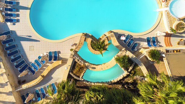An aerial view of a resort pool area with multiple sun loungers and a central swimming pool. - Xemxija Bay Hotel (St. Paul's Bay)