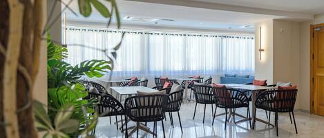 A modern dining area with a marble floor, black wicker chairs, and white tables.