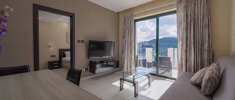 A modern living room with a glass coffee table, a sofa, a TV, and a balcony with curtains.