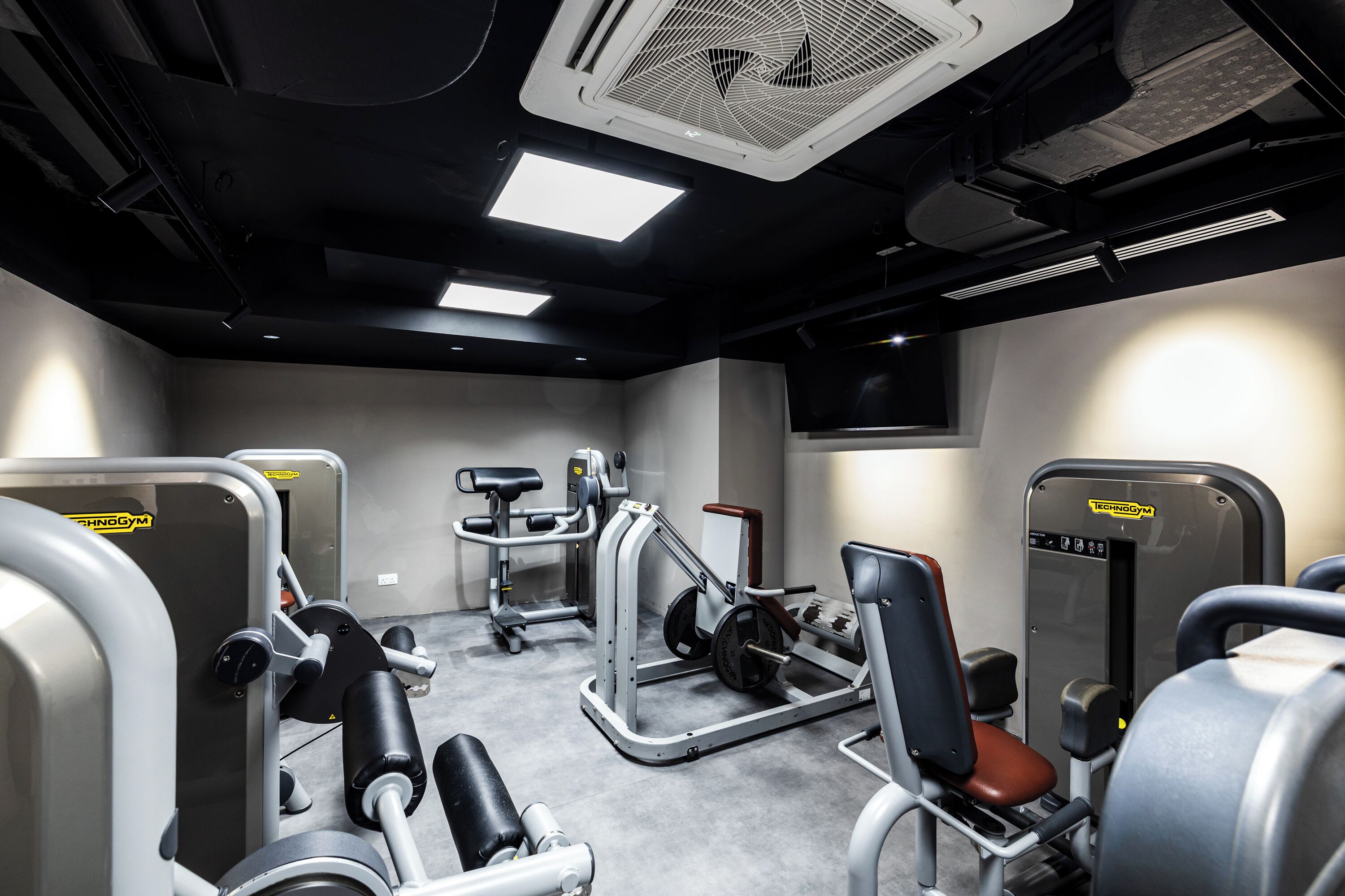 Un gimnasio con diversas máquinas de ejercicio, un televisor y un ventilador de techo.