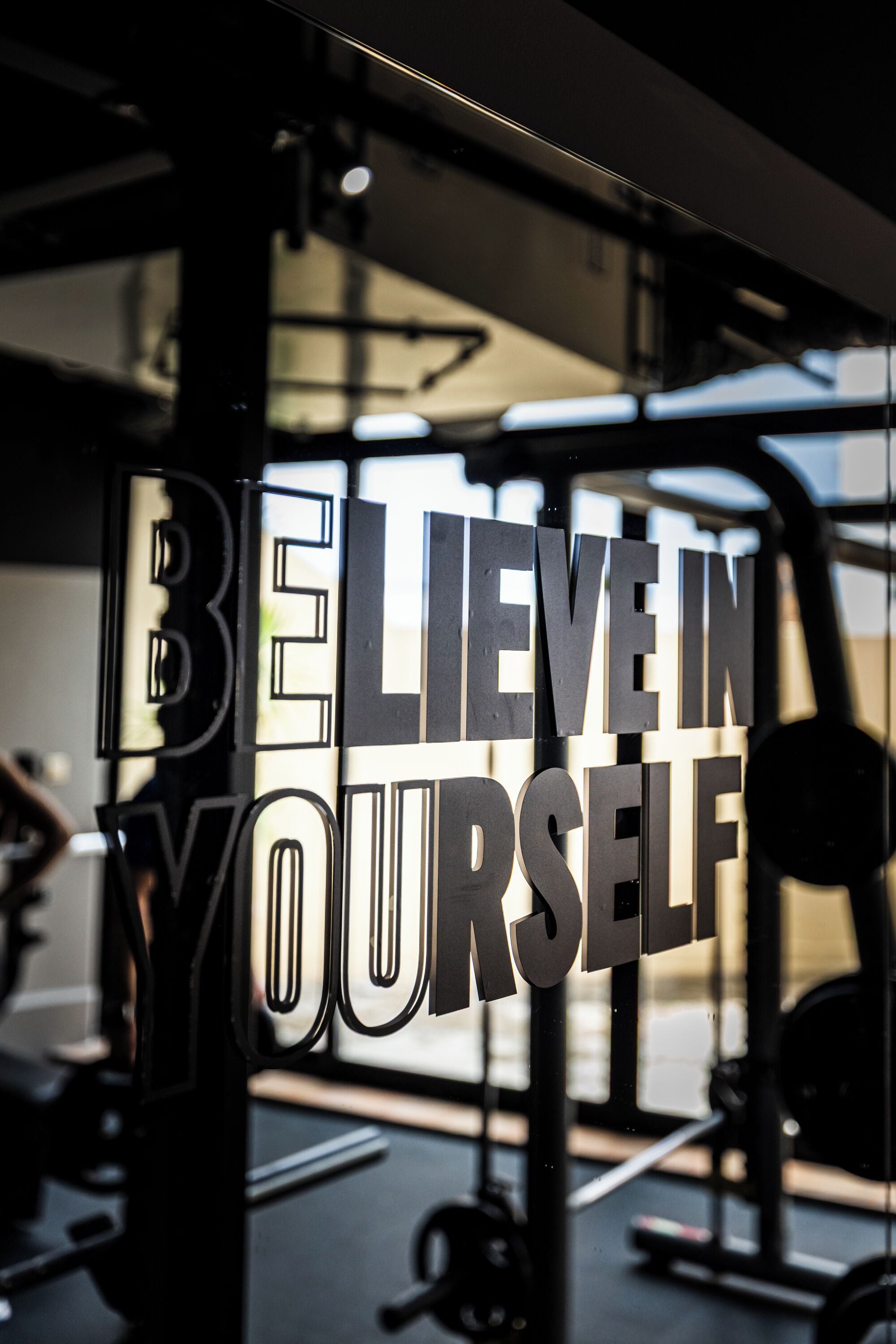 A motivational sign with the text 'BELIEVE IN YOURSELF' in a gym setting.