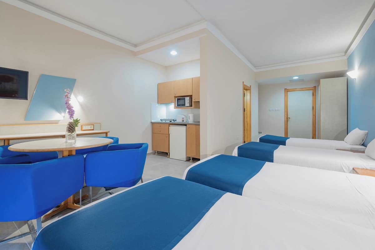 Een hotelkamer met kitchenette, een eethoek met blauwe stoelen en een bed met blauw-witte beddengoed.