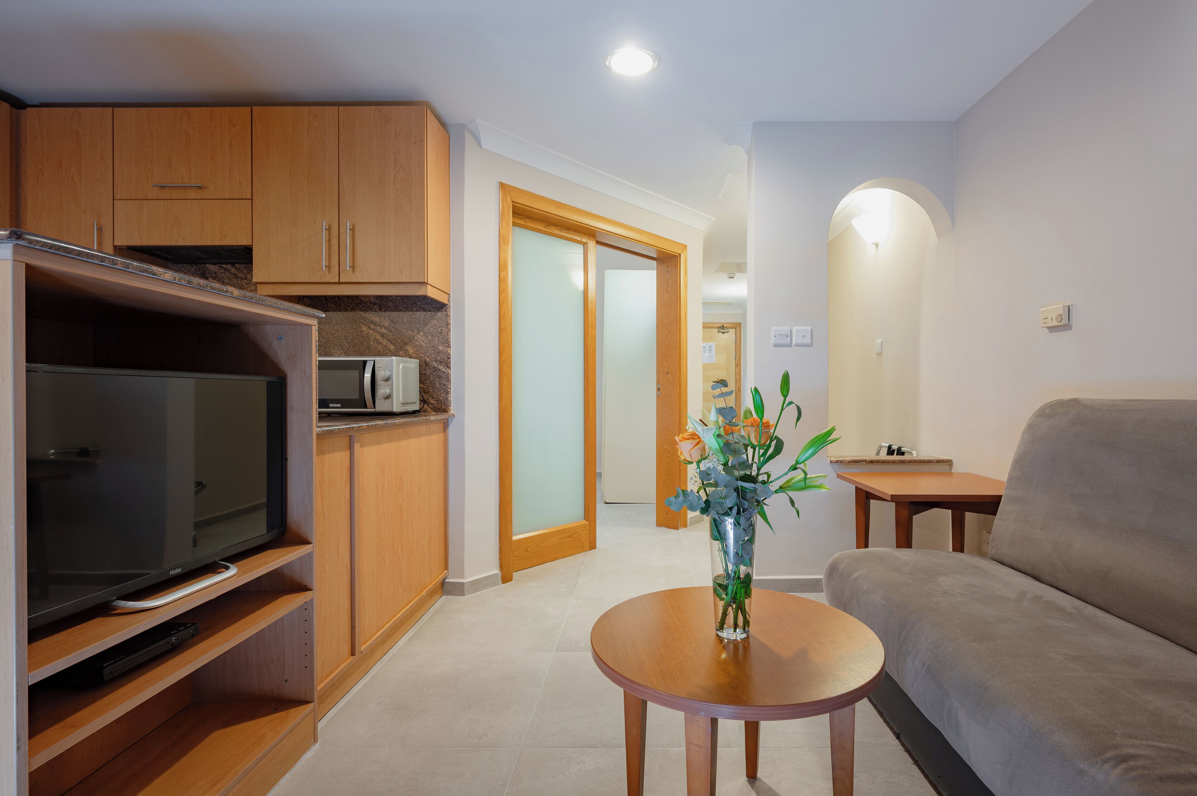 A modern living room with wooden cabinets, a flat-screen TV, a sofa, and a small table with a vase of flowers.