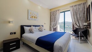 A modern hotel room with a large bed, a desk, and a view of the city. - Xemxija Bay Hotel (St. Paul's Bay)