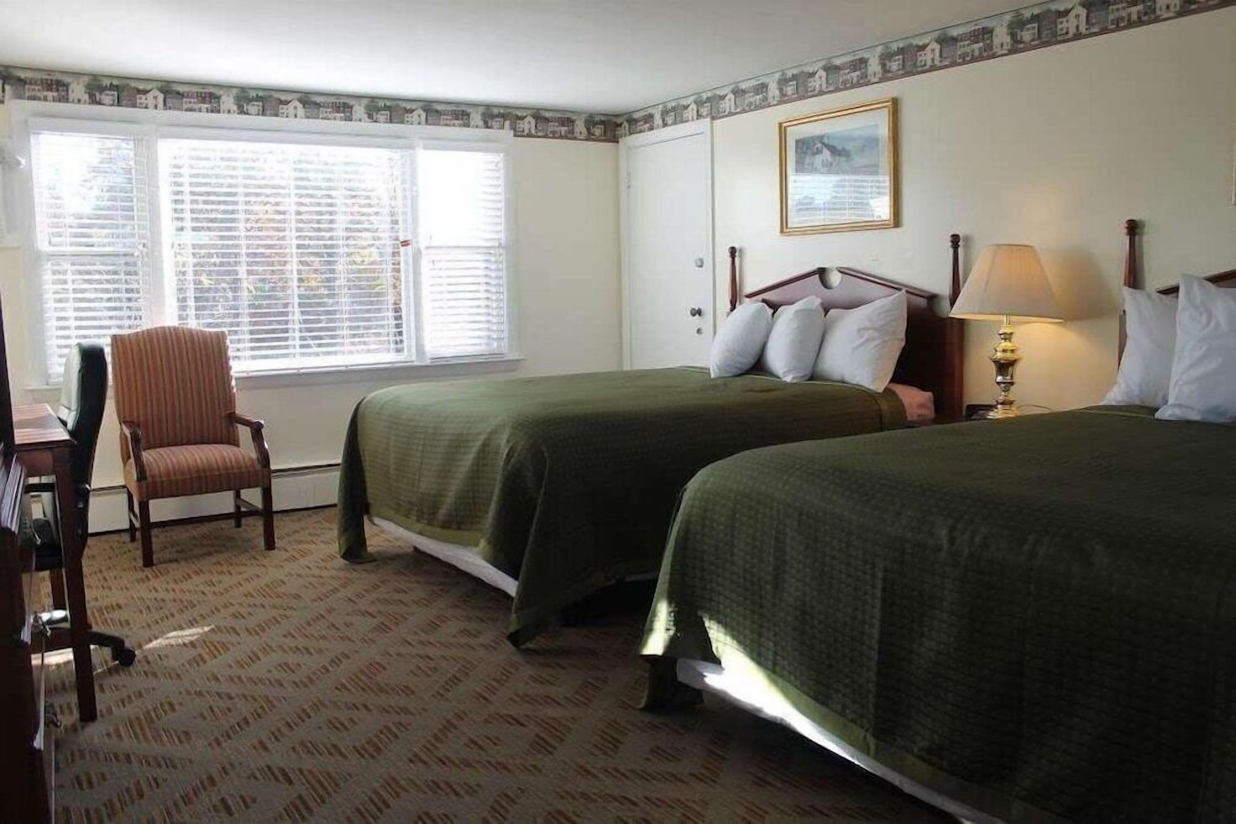 A hotel room with two beds, a desk, a chair, and a window with blinds.