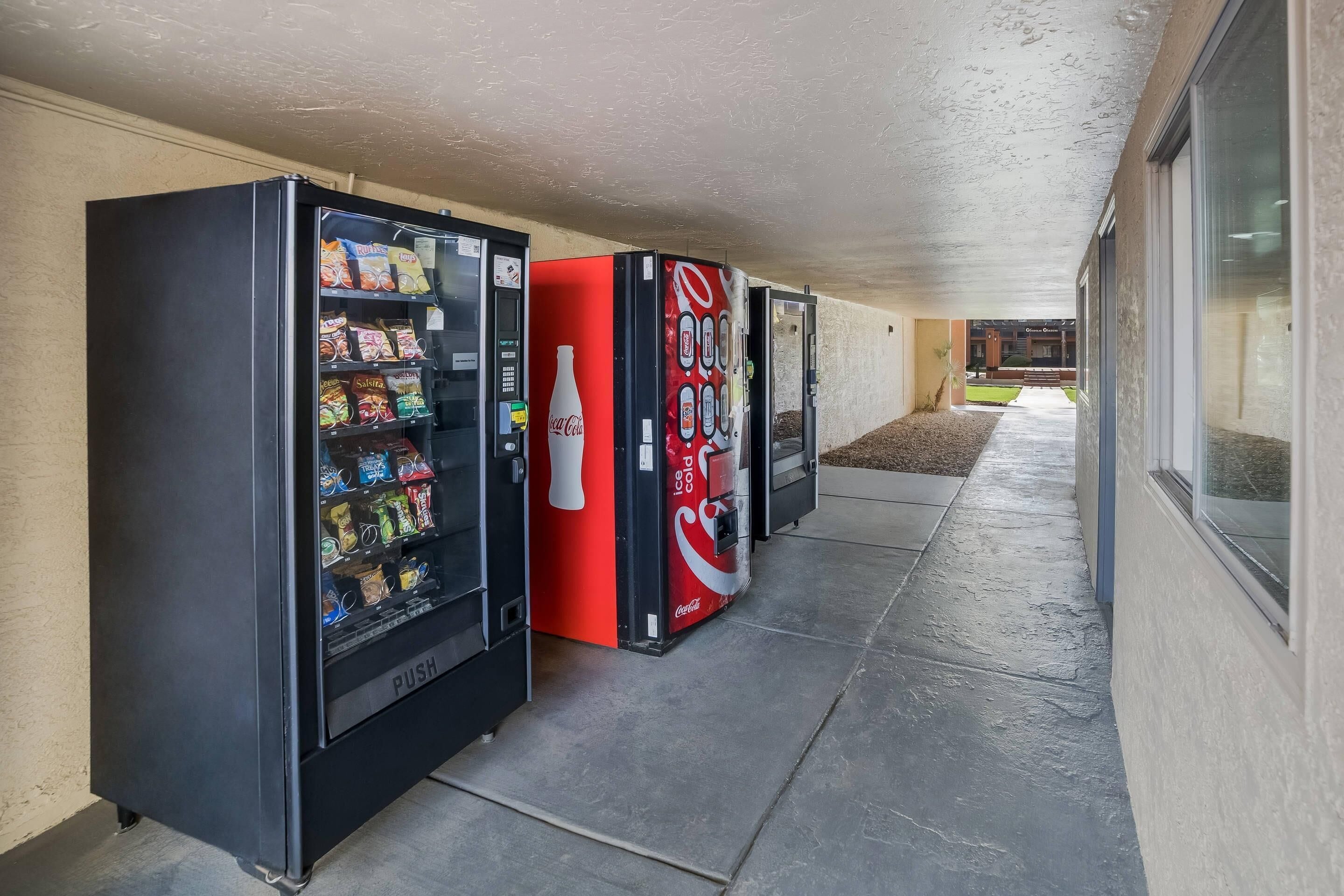 A row of vending machines with snacks and beverages, including Coca-Cola, along a covered walkway.