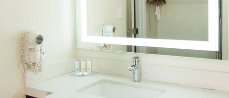 A bathroom with a large mirror, two sinks, a hairdryer, and a towel rack.
