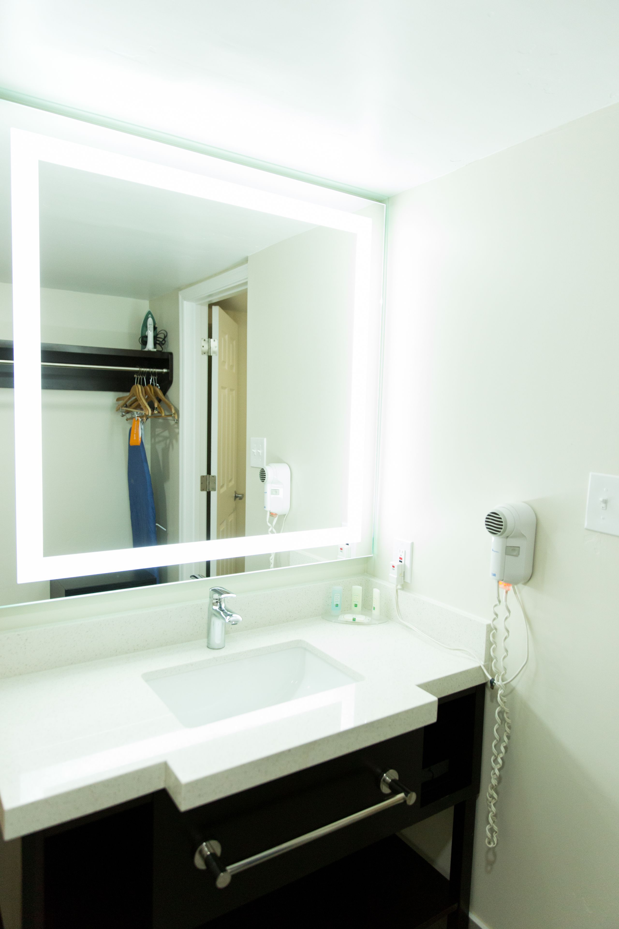 Un baño con un espejo grande, un lavabo blanco y un secador de pelo en la pared.
