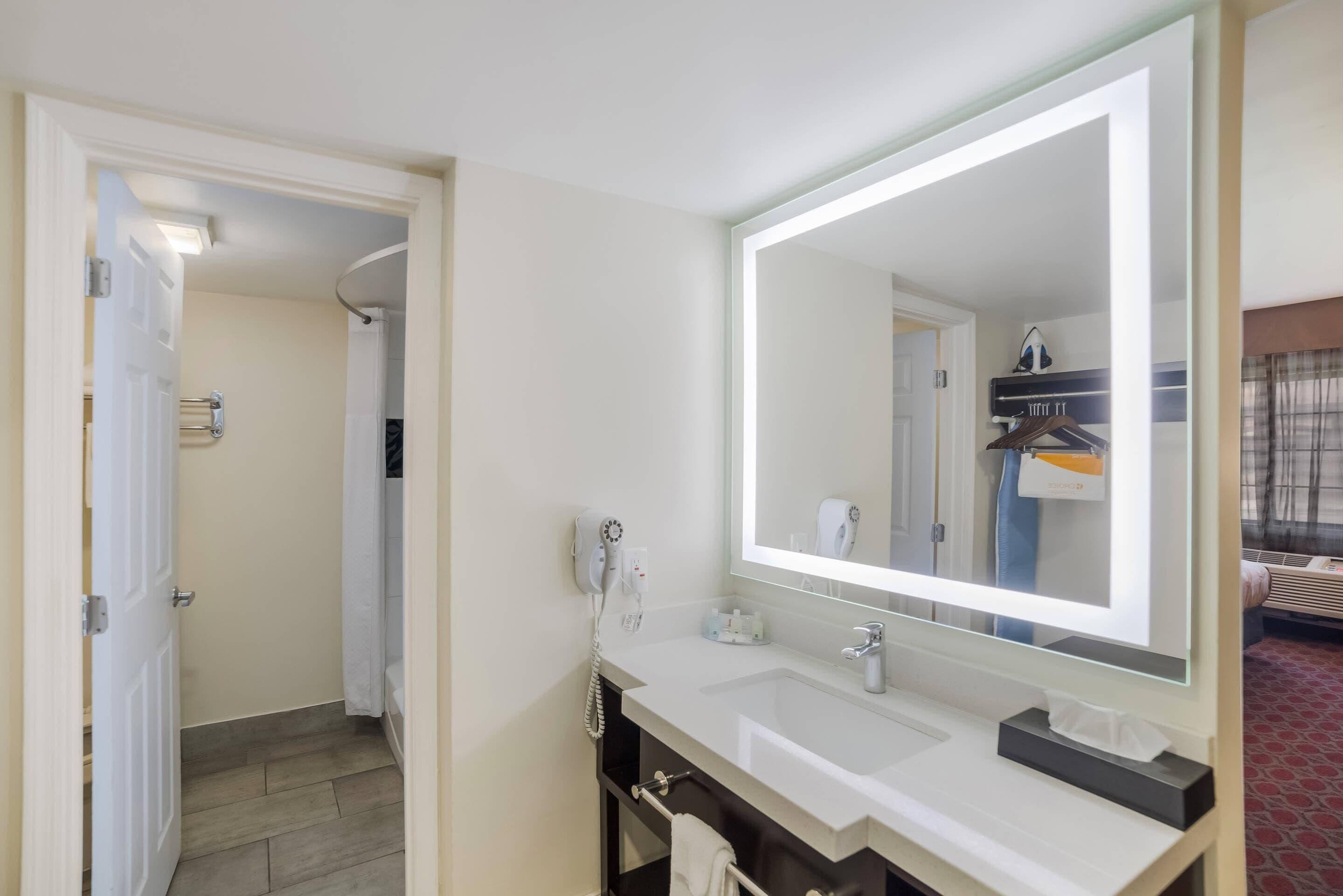 A hotel bathroom with a large mirror, a sink, and a shower area.