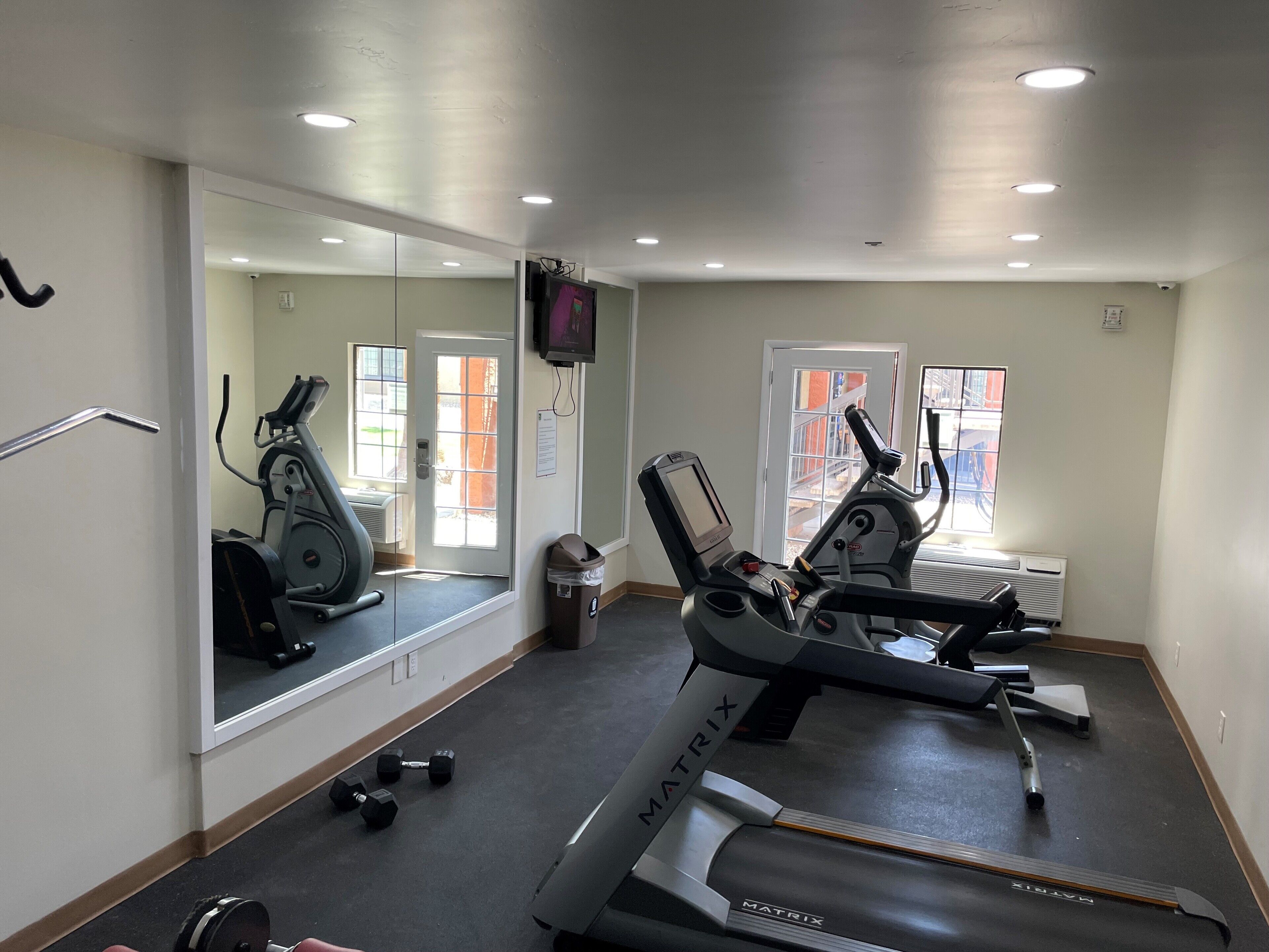 A gym with a treadmill, dumbbells, and a mirror.