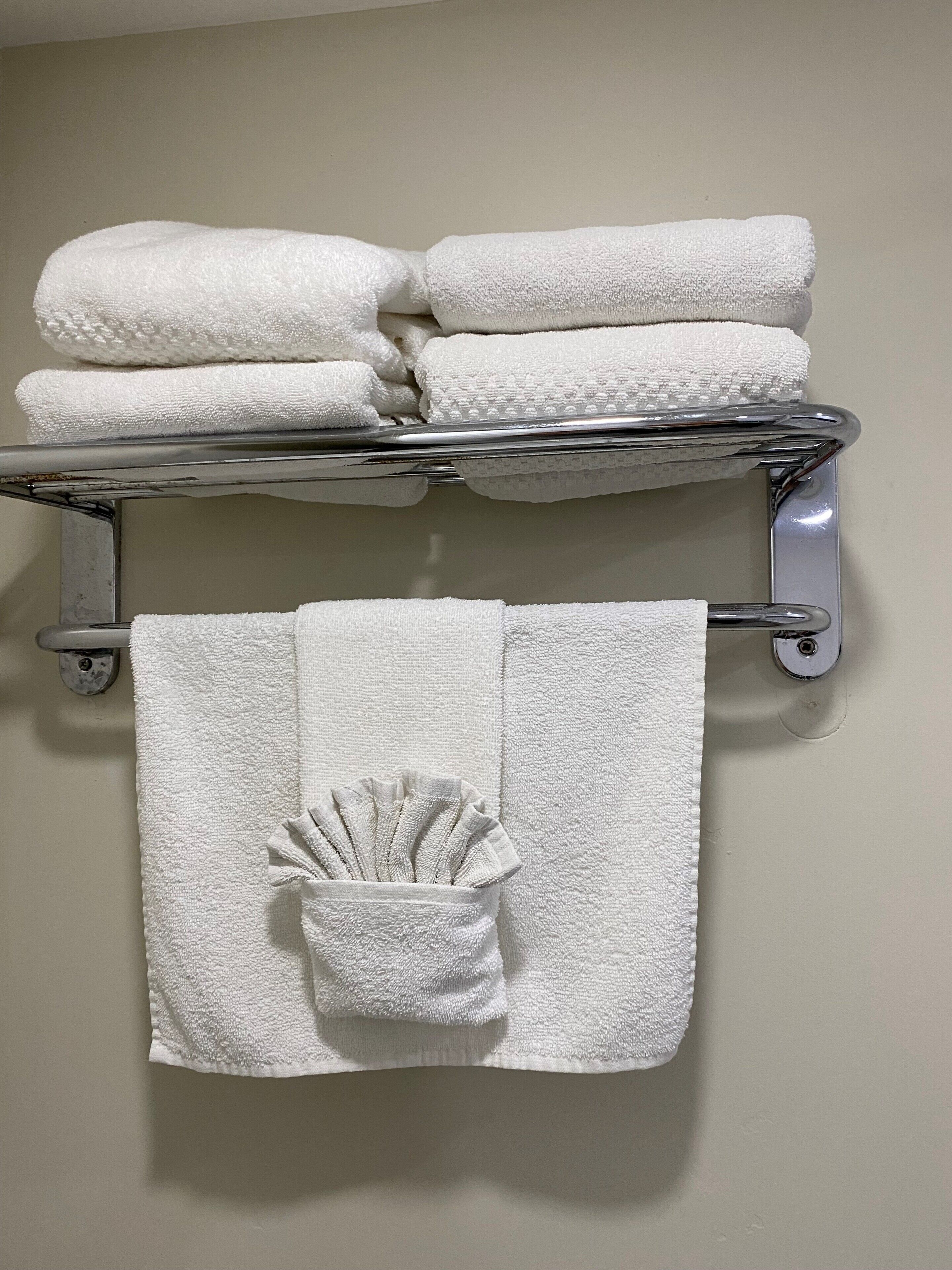 A bathroom with a towel rack holding three folded towels and a single towel with a decorative fan.