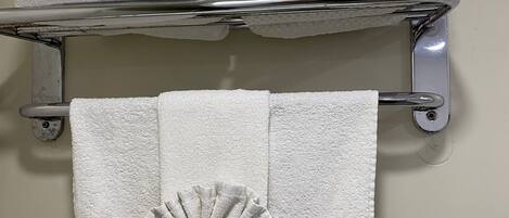 A bathroom with a towel rack holding three folded towels and a single towel with a decorative fan.