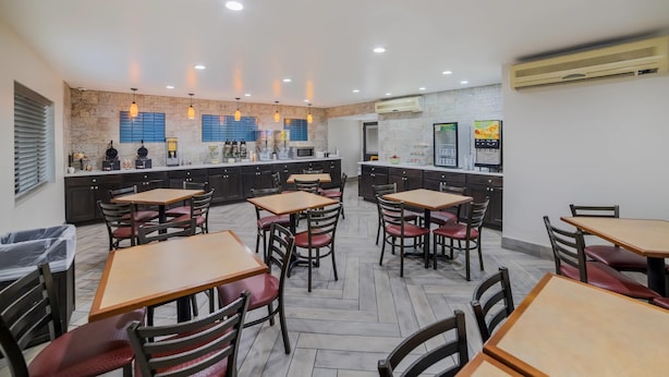 Un restaurant doté de plusieurs tables et chaises, d’un espace cuisine et d’un appareil de climatisation fixé au mur.