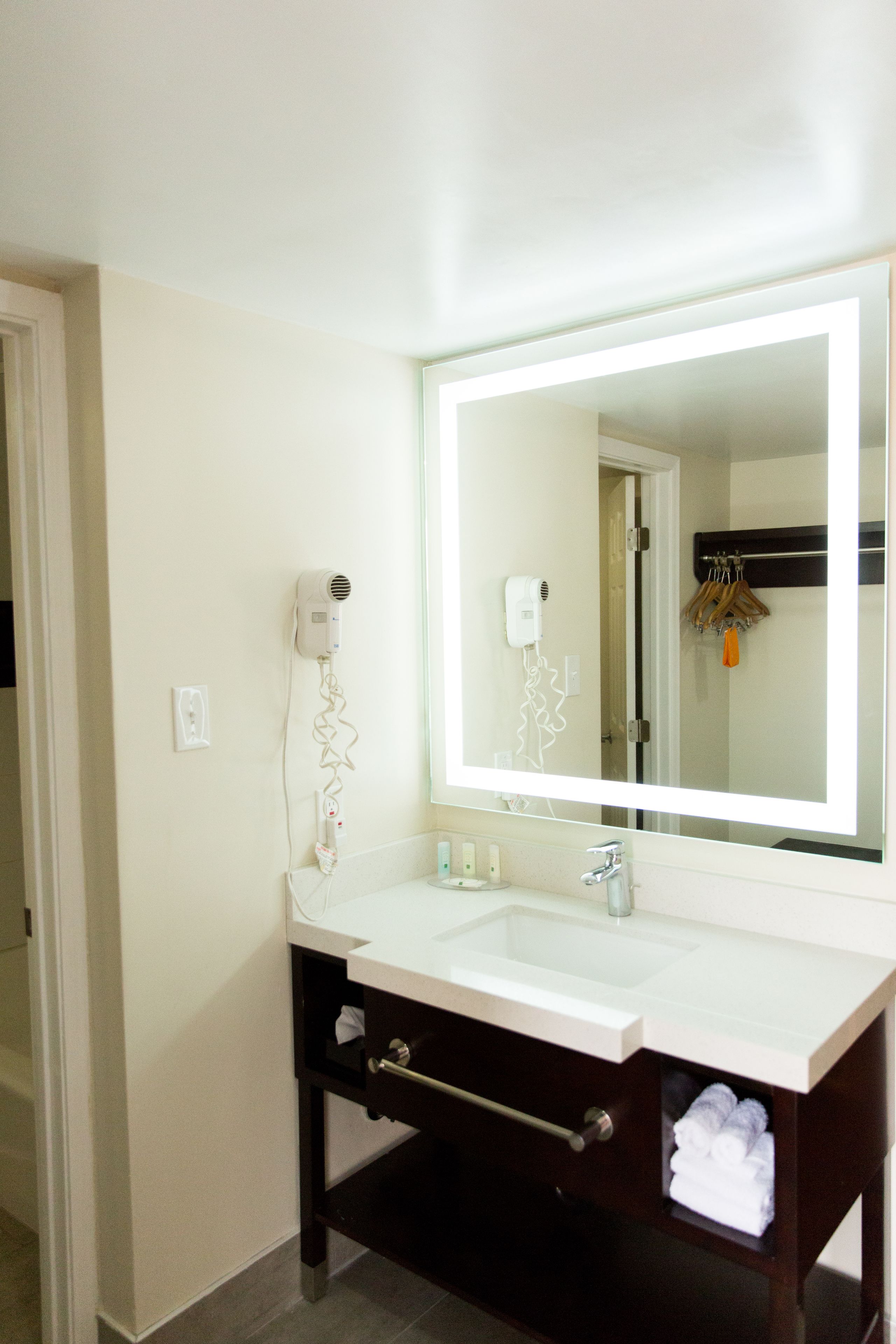 A bathroom with a white sink, a large mirror, and a hairdryer on the wall.