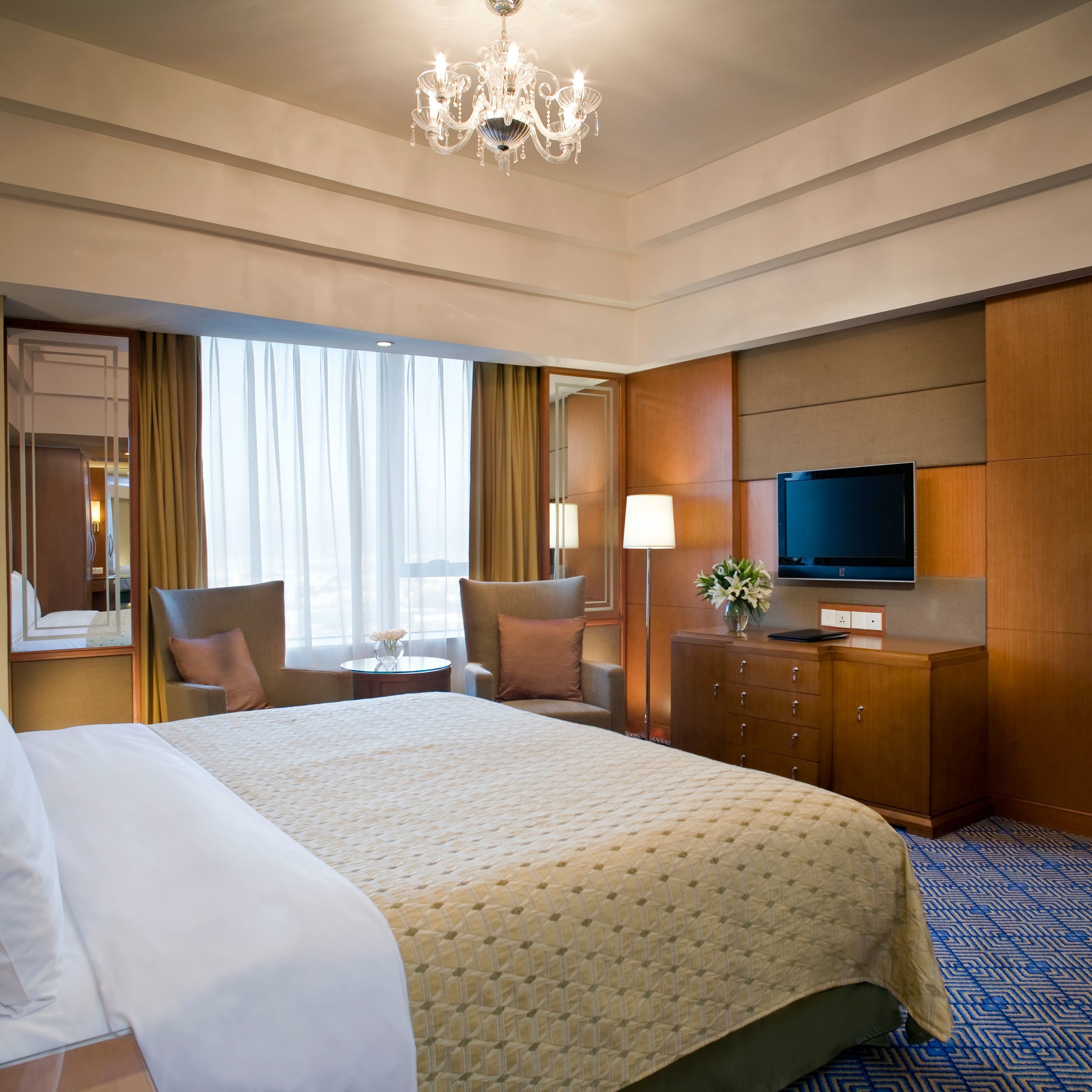A hotel room with a large bed, a television, a desk with a lamp, and a mirror.