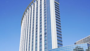 A modern hotel with a curved glass facade, parked cars, and a clear blue sky. - Shangri-La Baotou (Baotou)