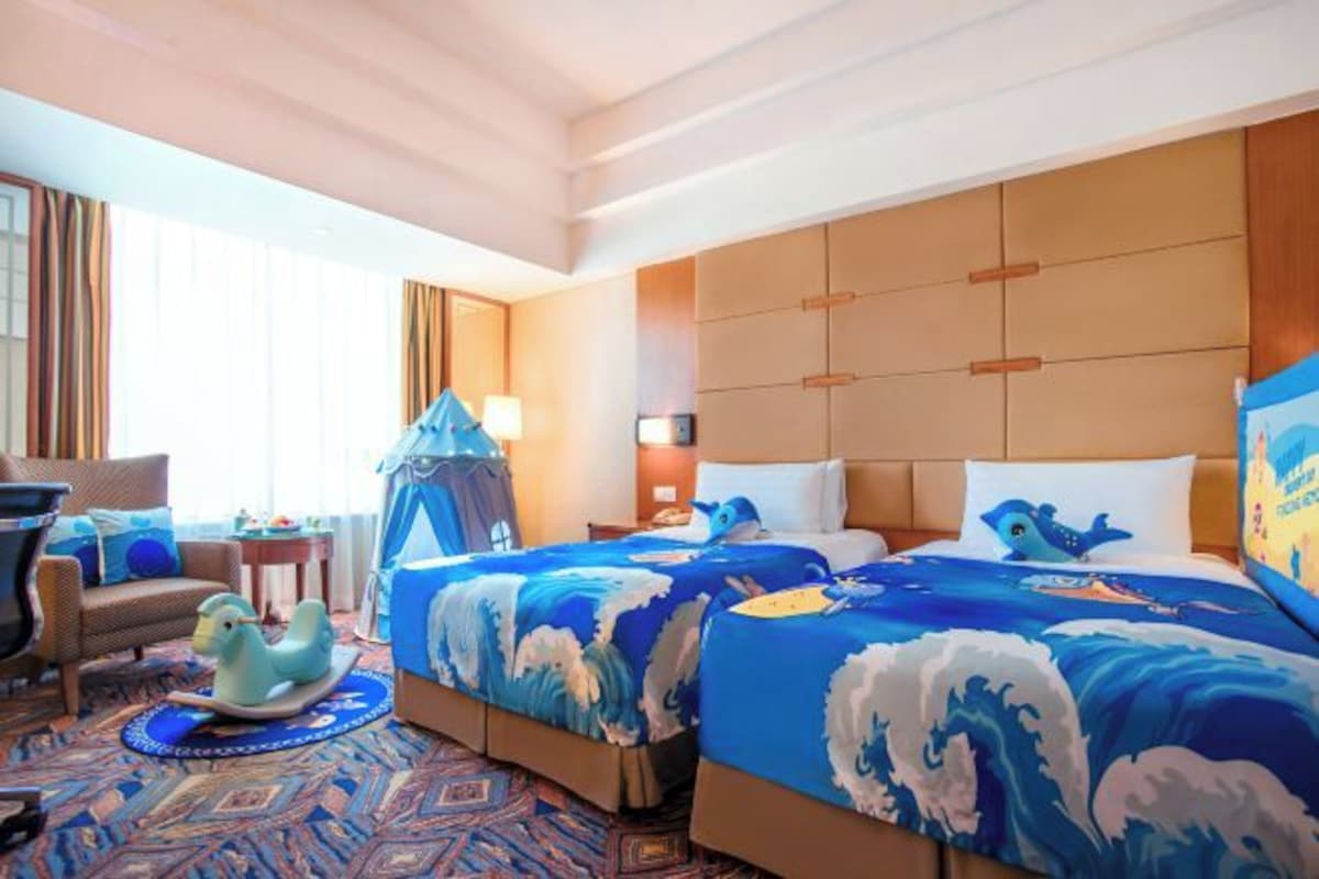 A hotel room with two beds, a sofa, a rocking horse, and a patterned carpet.