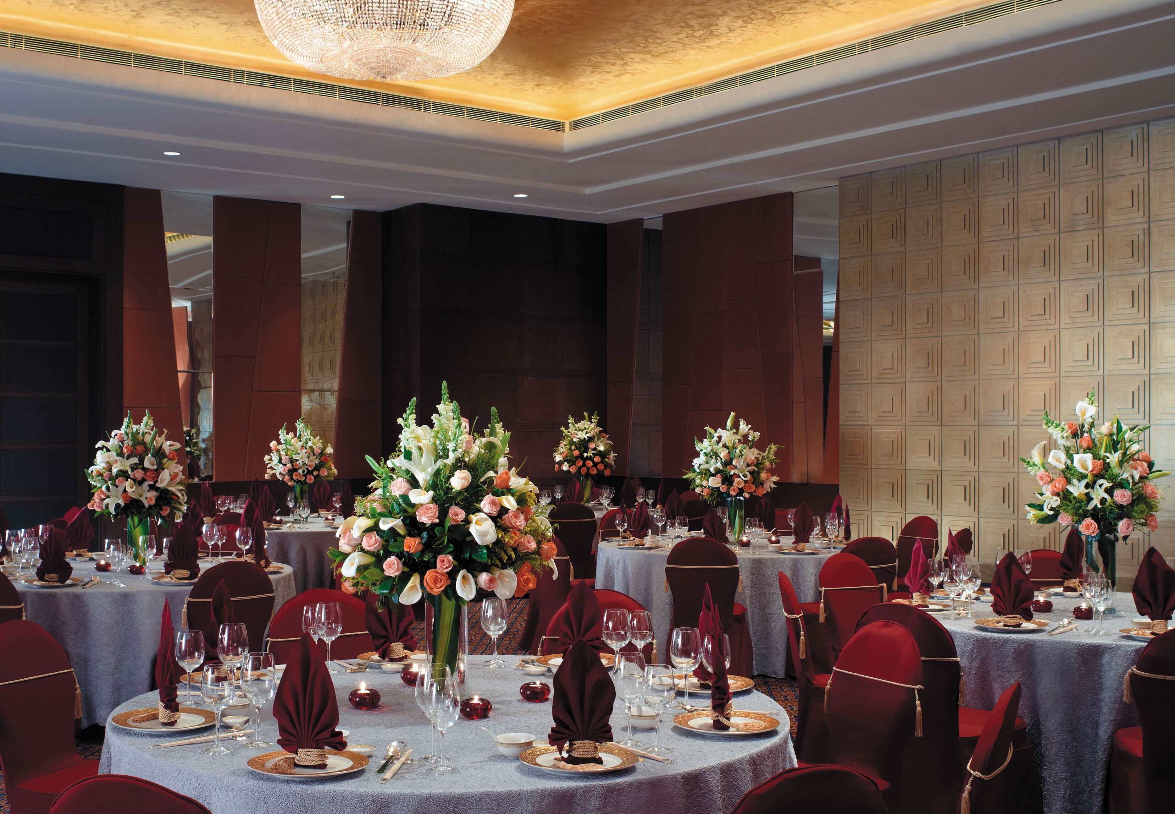 A banquet hall with round tables set for dining, each with floral centerpieces and red chairs.