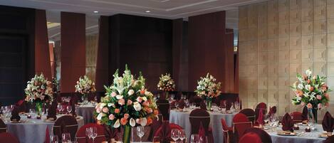 A banquet hall with round tables set for dining, each with floral centerpieces and red chairs.
