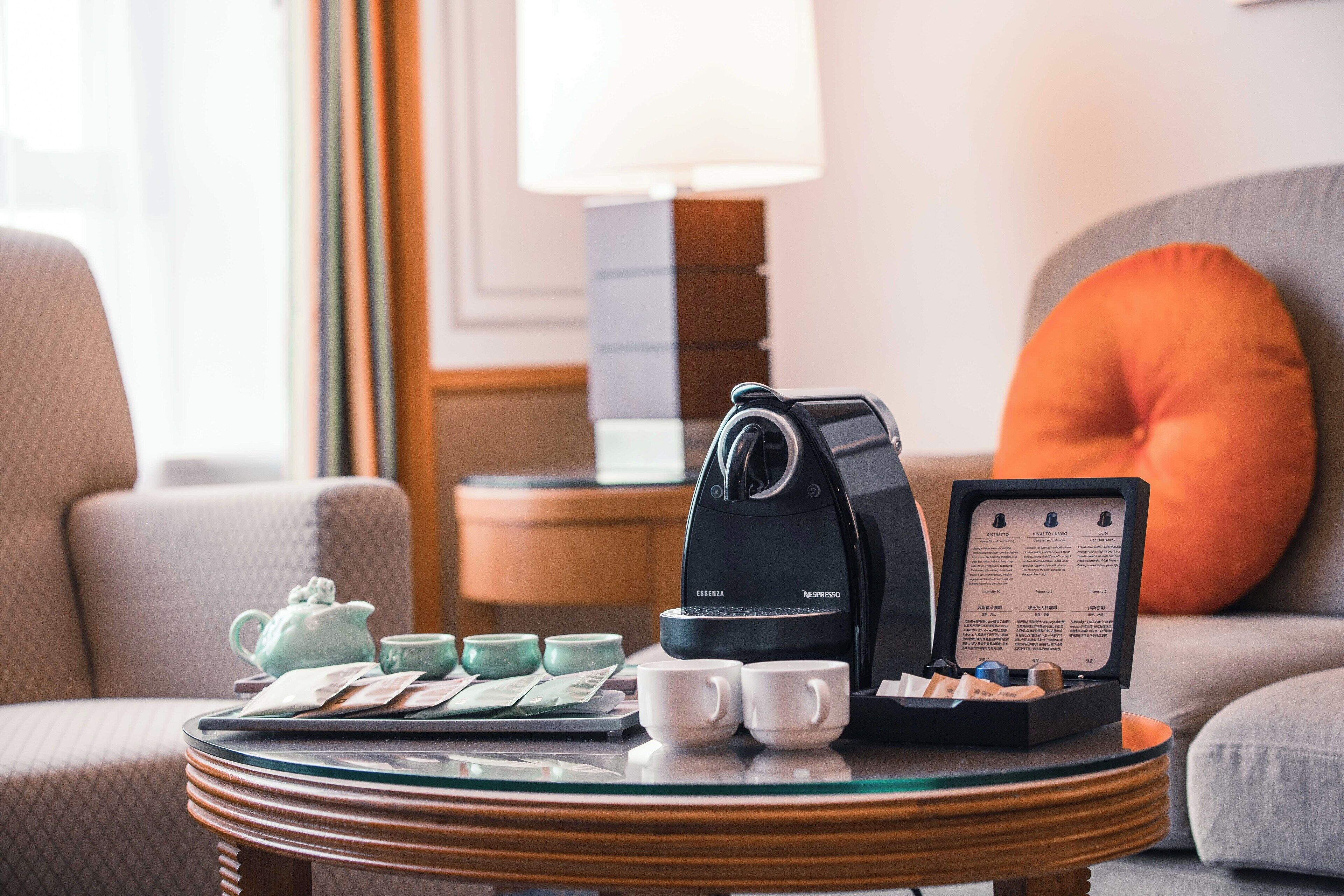 Eine Kaffeemaschine, ein Teekessel, Tassen und eine Speisekarte stehen auf einem Tisch in einem Hotelzimmer.