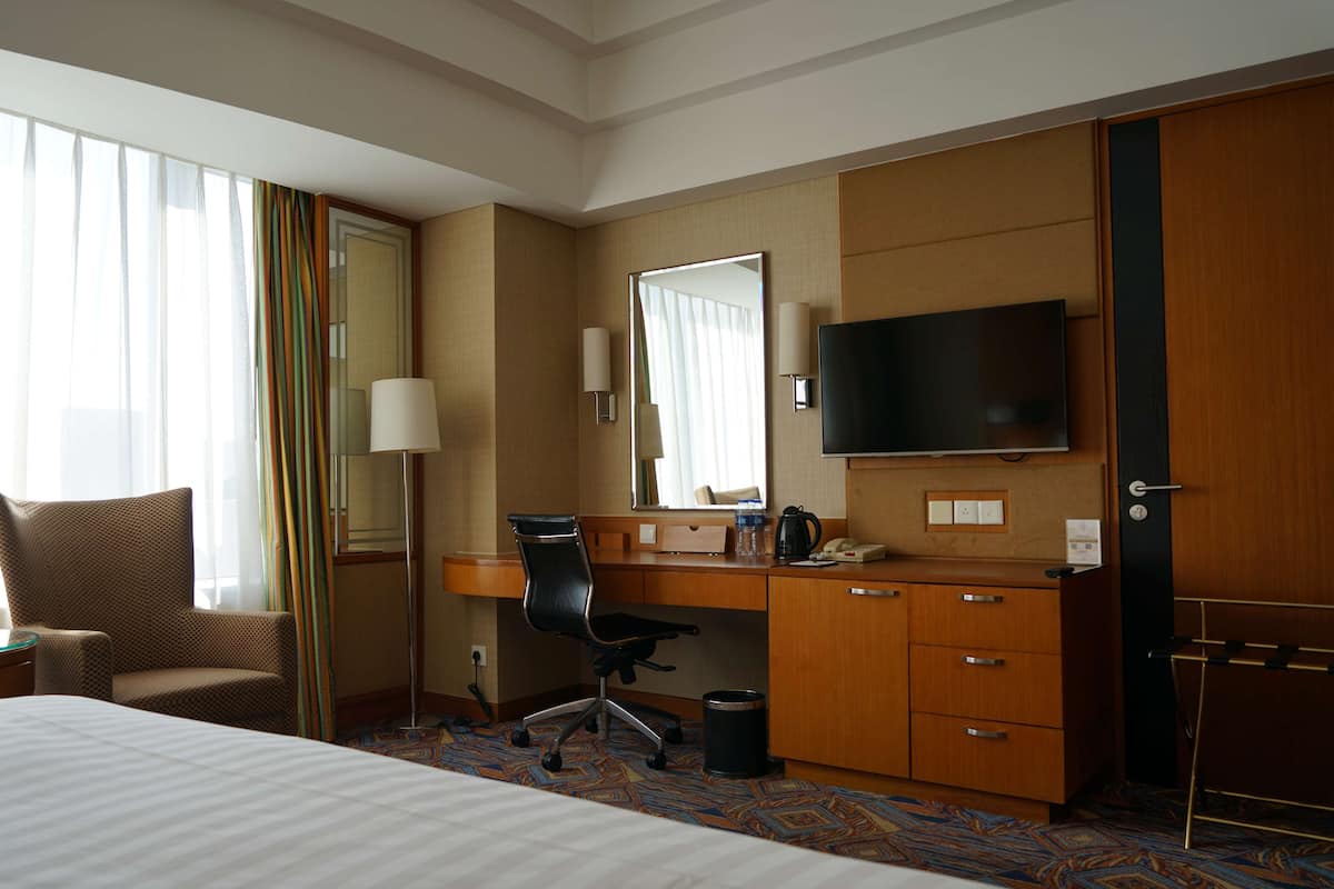A hotel room with a bed, a desk, a chair, a TV, and a wardrobe.