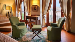 A cozy room with a staircase, green armchairs, a small table with a lamp, and a view through large windows. - Resort Locanda San Verolo Boutique Hotel (Costermano sul Garda)