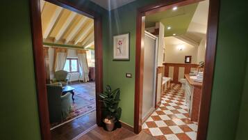 A hallway with a checkered floor leading to a bathroom and a living area with a sofa and curtains.
