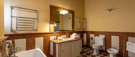A bathroom with a checkered floor, a sink, a toilet, a bidet, a bathtub, and a mirror with lights.