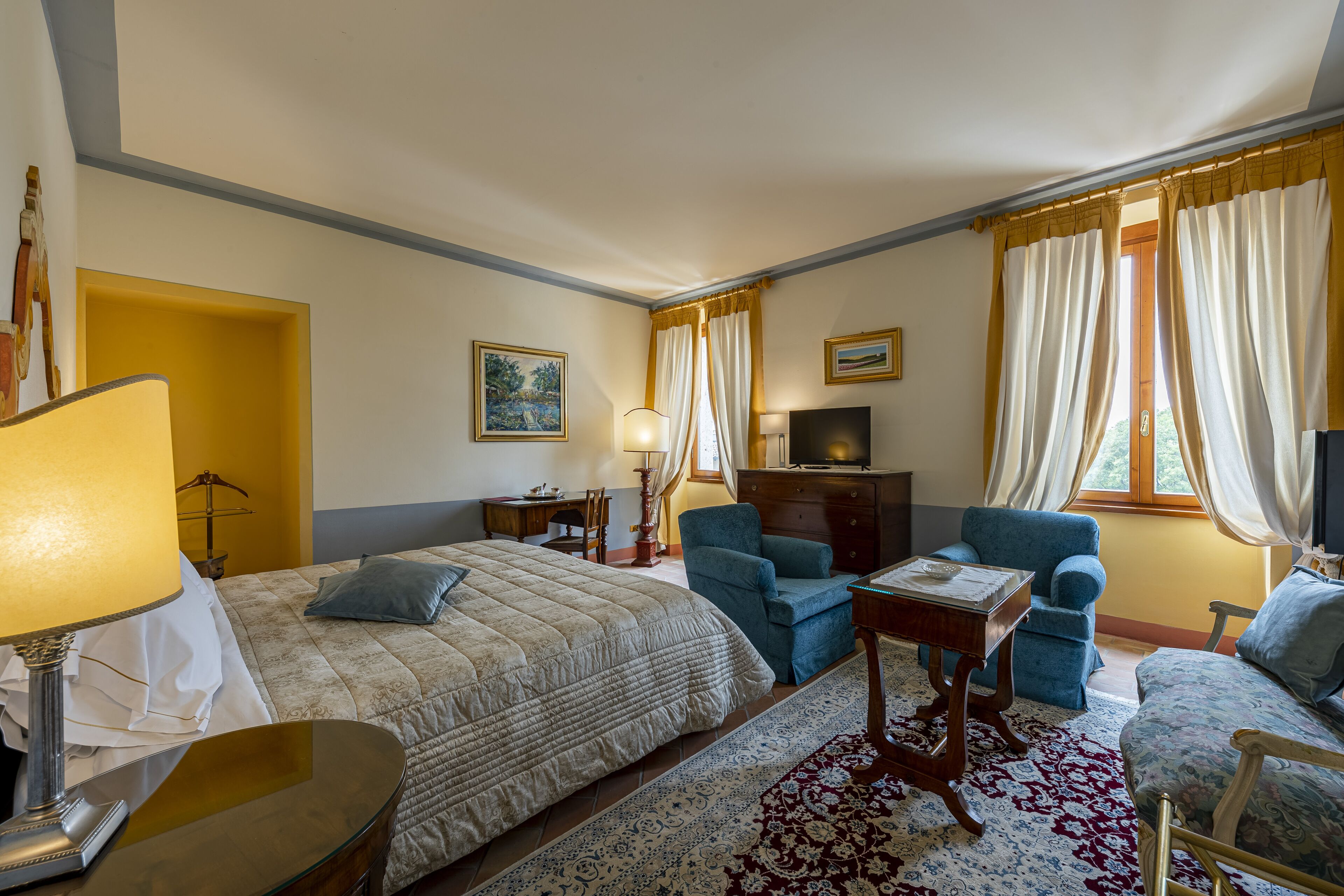 Ein Hotelzimmer mit einem Bett, zwei Sesseln, einem kleinen Tisch, einem Fernseher und einer Lampe.