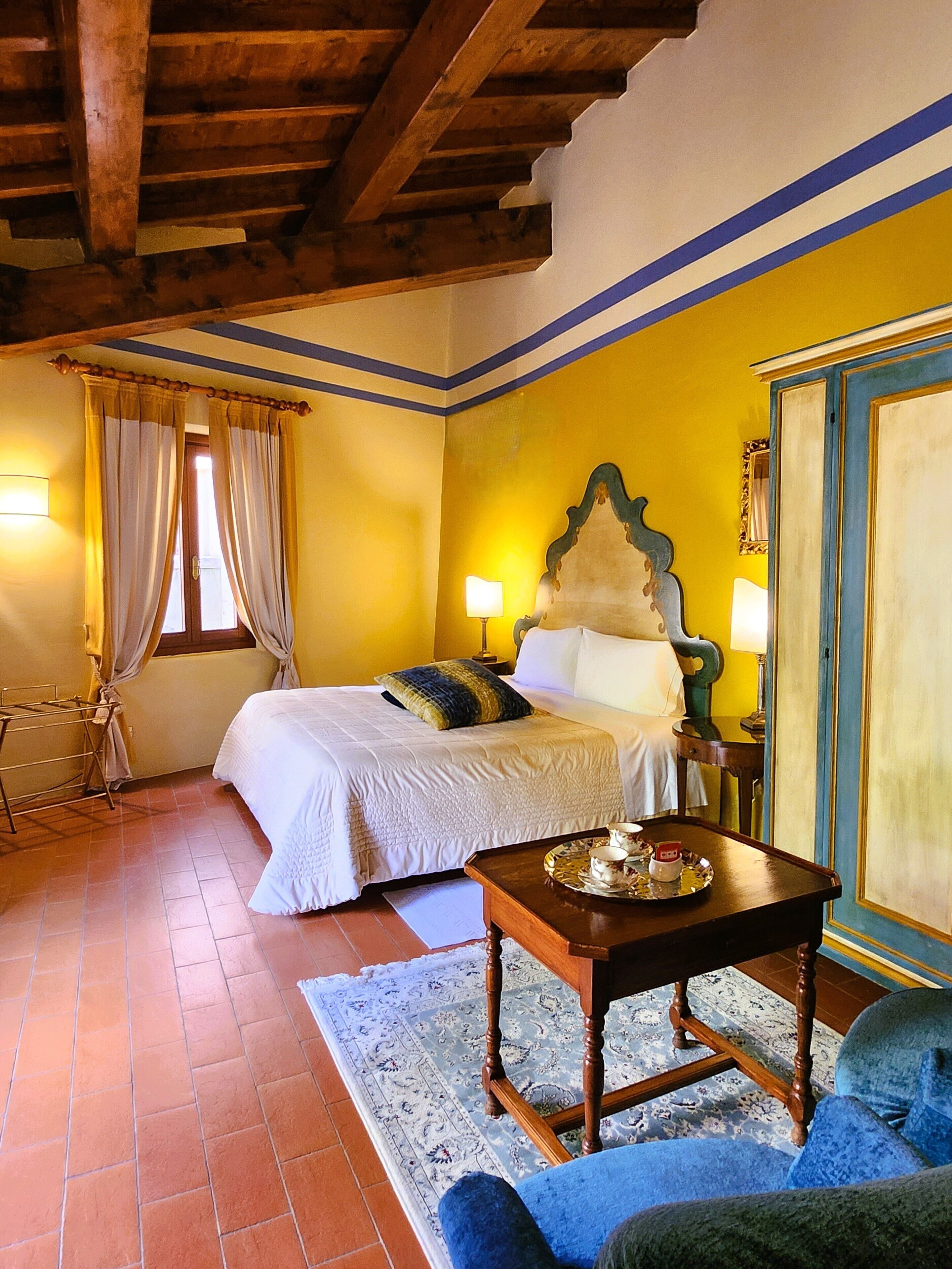 Quarto com cama, luminárias de cabeceira, painel de cabeceira em madeira, mesa de cabeceira, sofá azul e tapete estampado.