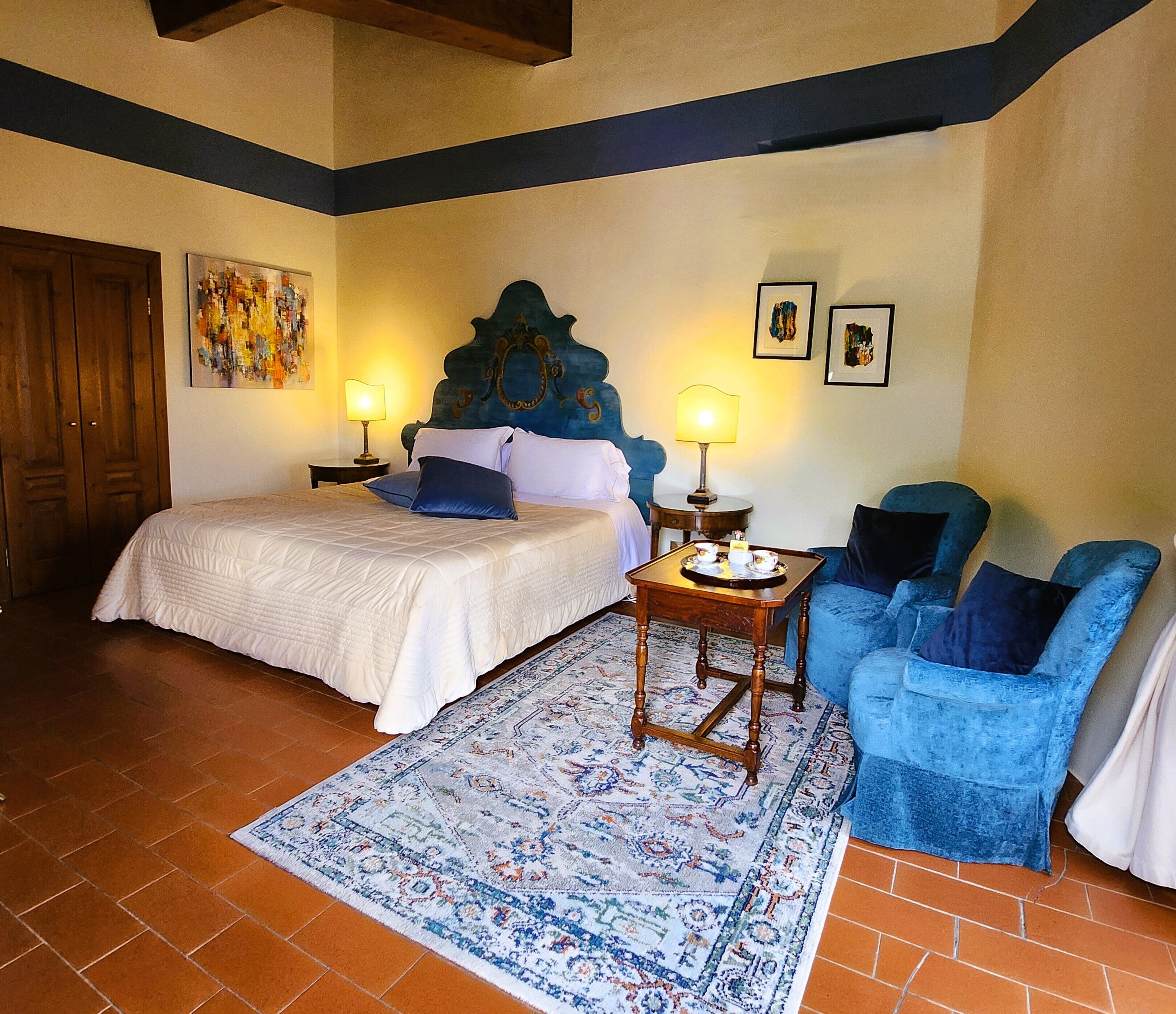 A bedroom with a bed, two bedside tables with lamps, a blue armchair, a patterned rug, and a wooden headboard.