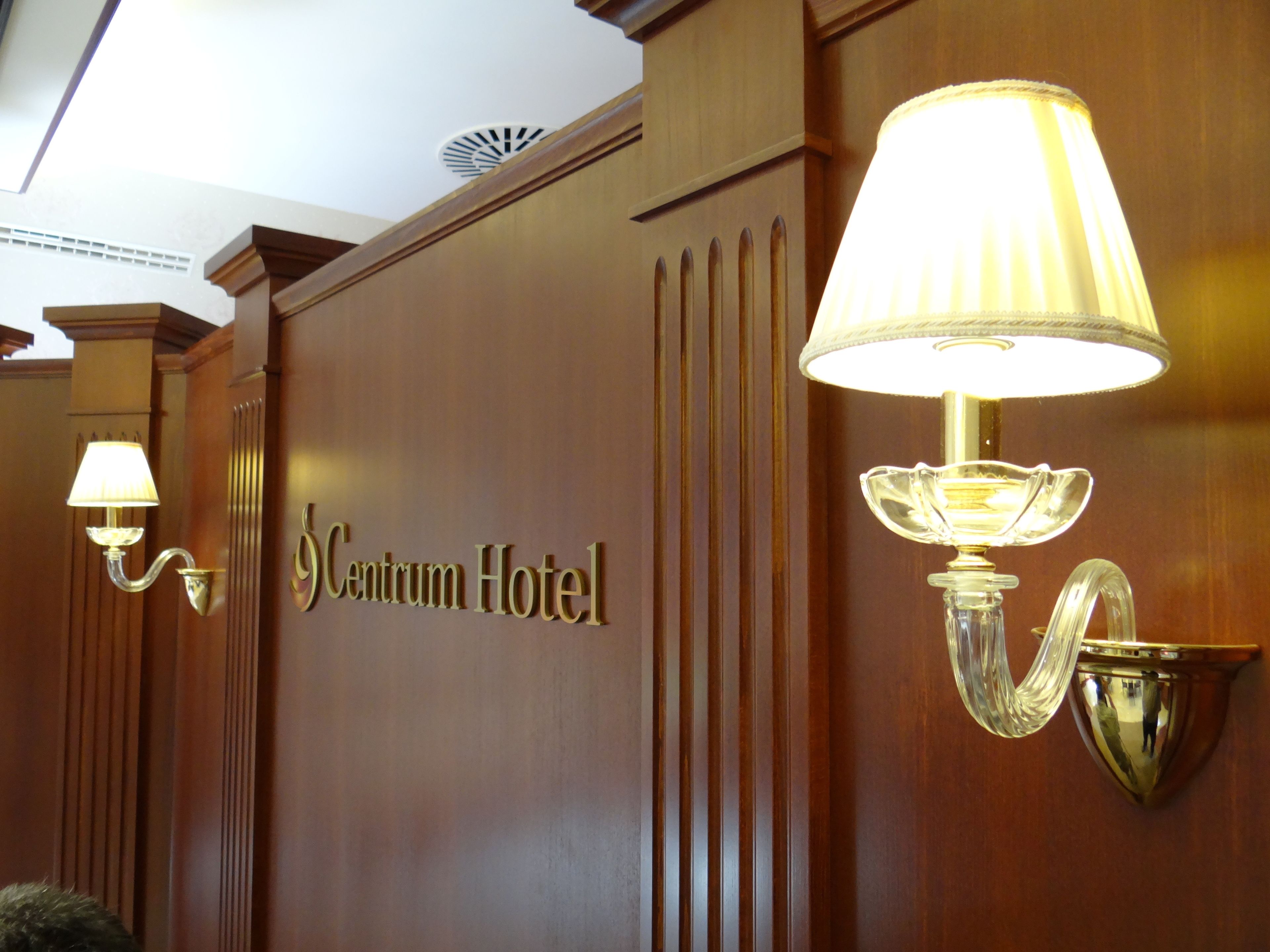 A hotel entrance with a sign reading "Centrum Hotel" and two wall-mounted lamps.