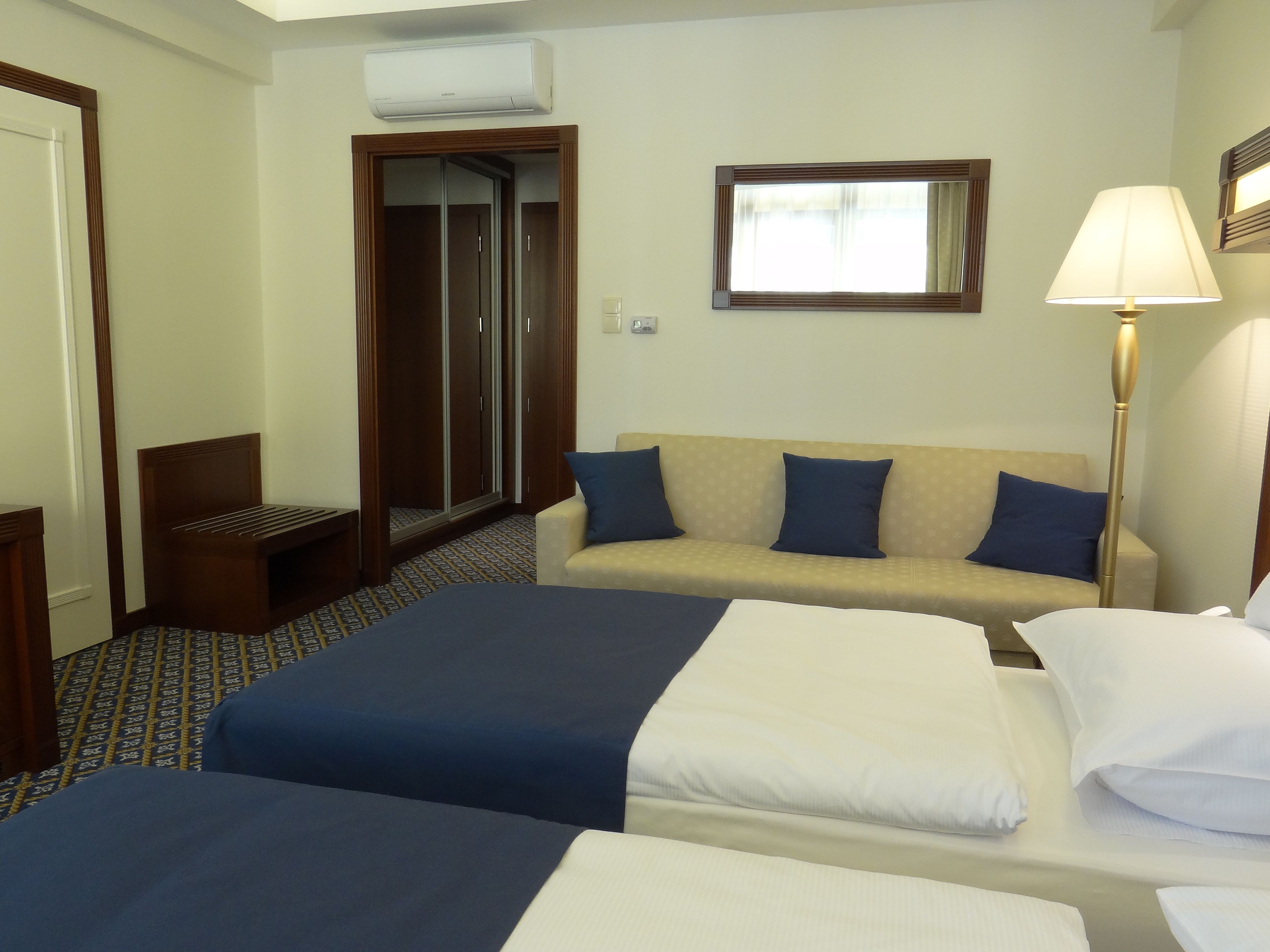 Habitació d'hotel amb dos llits, un sofà, un armari i una làmpada.