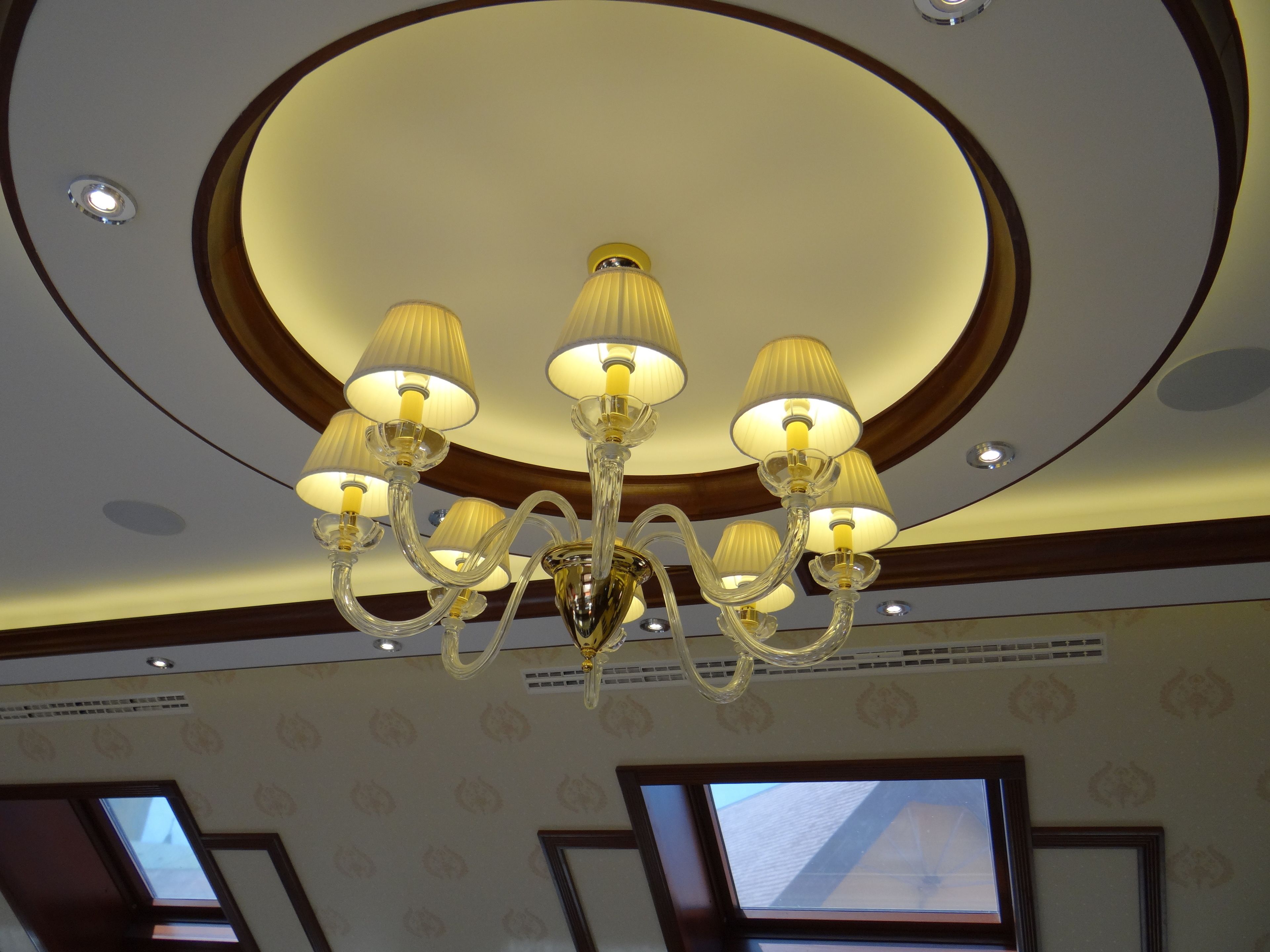 A chandelier with multiple light fixtures in a room with patterned wallpaper and skylights.
