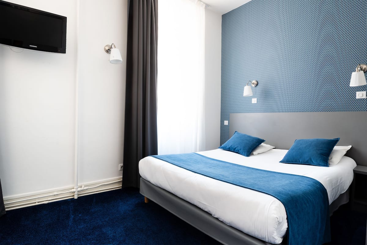 A modern hotel room with a large bed, a flat-screen TV mounted on the wall, and a patterned accent wall.