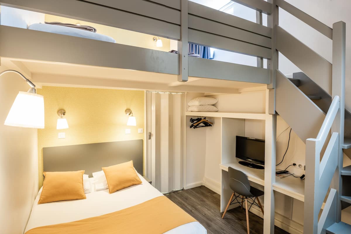 A modern hotel room with a bunk bed, a desk with a computer, and a staircase.