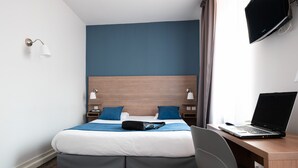 A hotel room with a bed, a desk with a laptop, a chair, and a TV on the wall. - Hotel Au Patio Morand (Lyon)