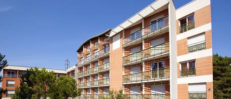 A multi-story residential building with balconies, a flat roof, and a clear blue sky.