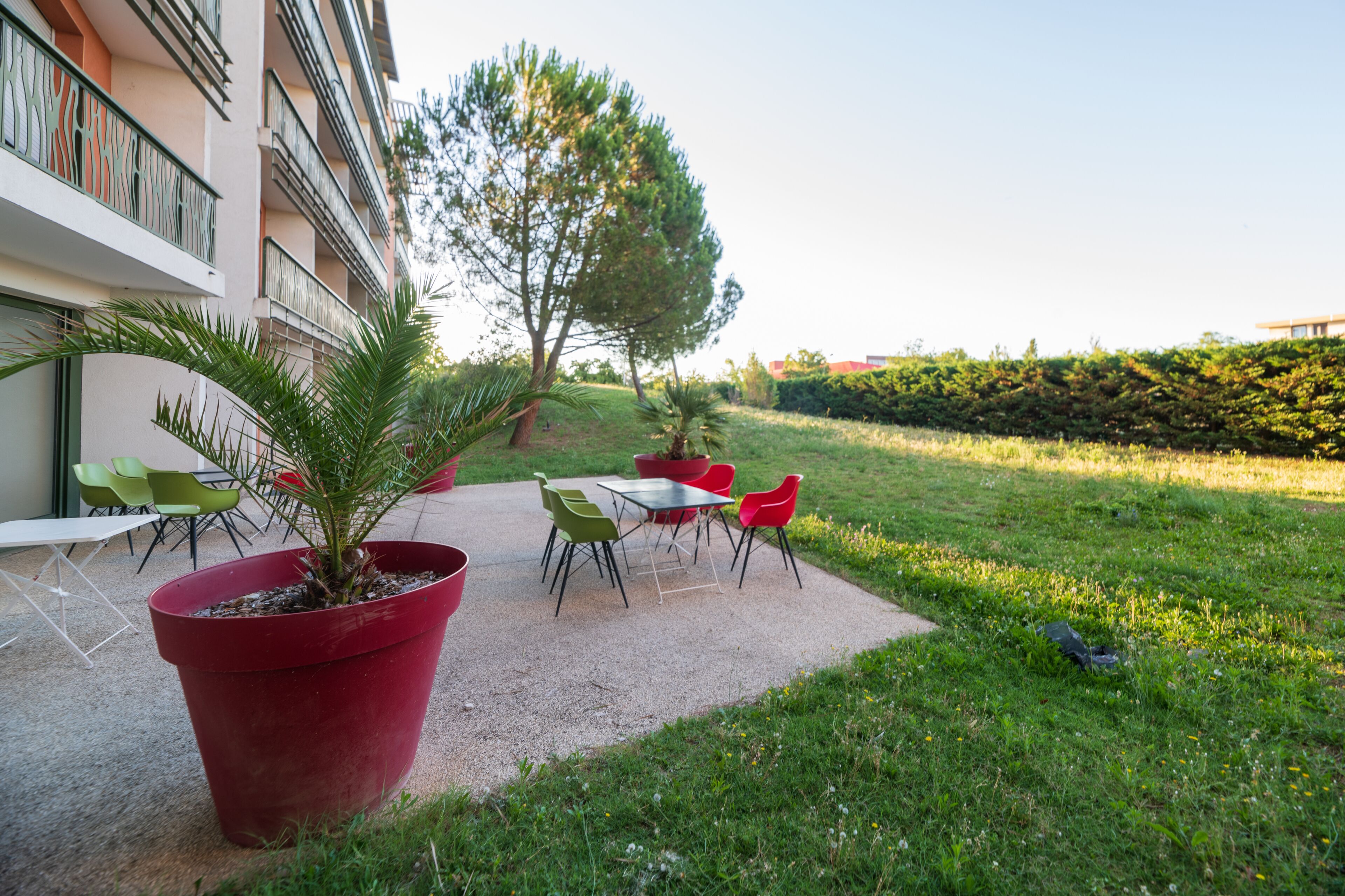 An outdoor patio area with a gravel path, green and red chairs, and potted plants.