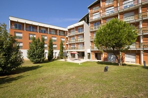 A multi-story residential building with balconies, a central courtyard with seating, and surrounding greenery.