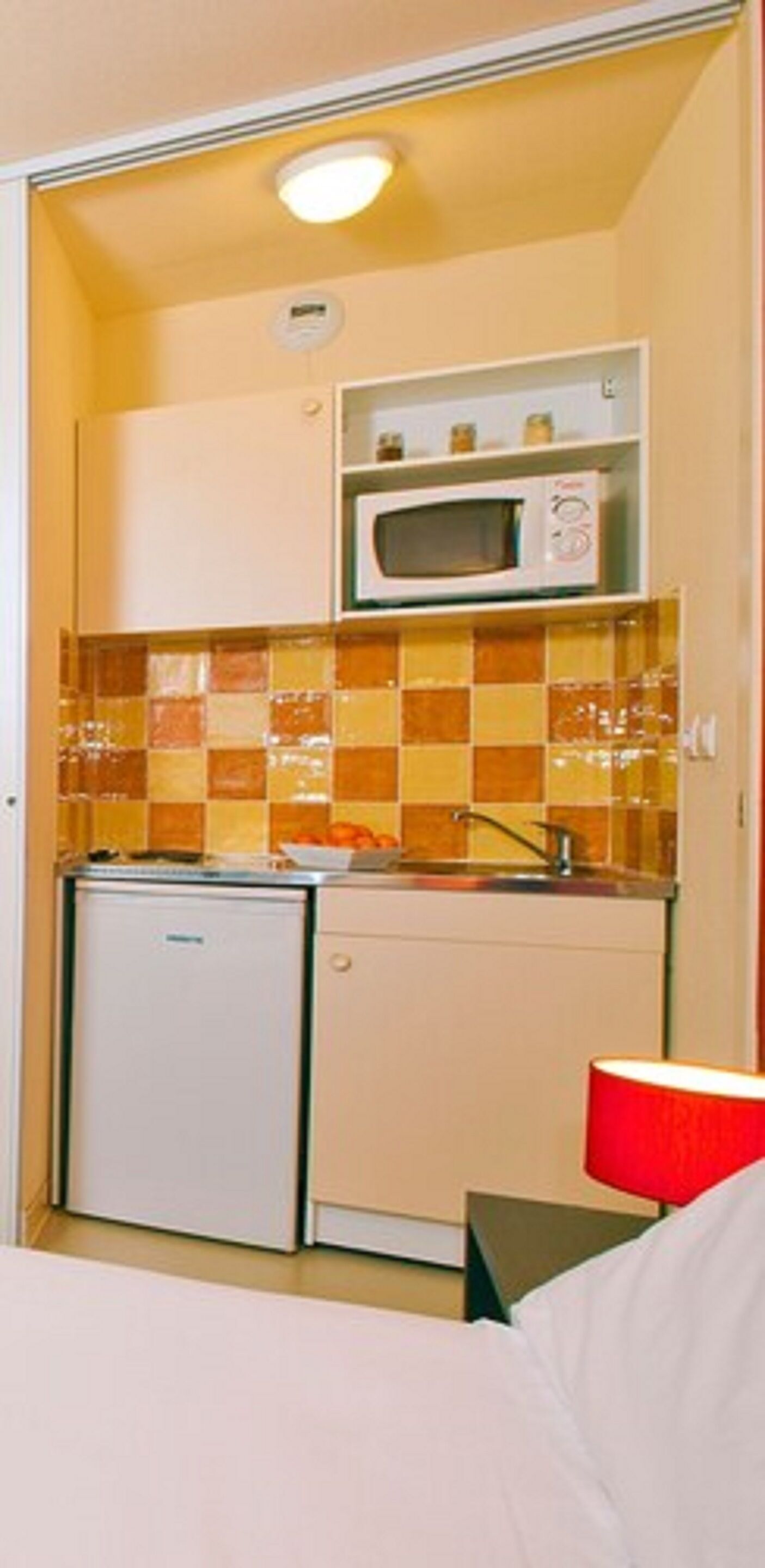 A compact kitchenette with a microwave, a small refrigerator, and a tiled backsplash.